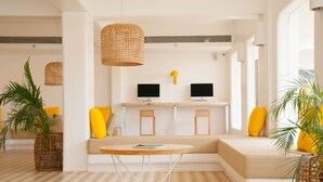 A modern living room with a sofa, a round table, two monitors on a shelf, and a hanging wicker light fixture.