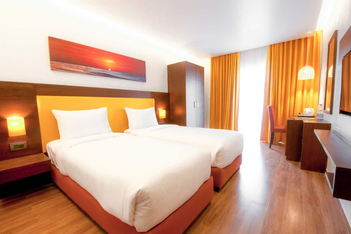 Habitación de hotel con dos camas, un escritorio, una silla, un espejo y un cuadro en la pared.