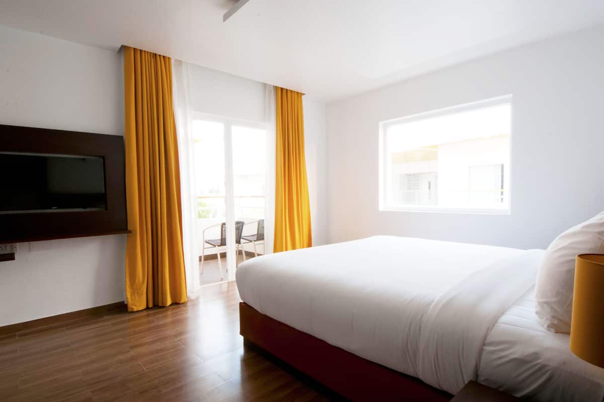 Una habitación de hotel con una cama grande, un televisor de pantalla plana montado en la pared y una ventana con cortinas.