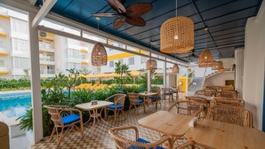 A rooftop bar with wicker furniture, a pool, and a view of the hotel building.