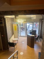 Entrada de un hotel con mostrador de recepción, zona de estar con un banco y vistas al patio exterior.