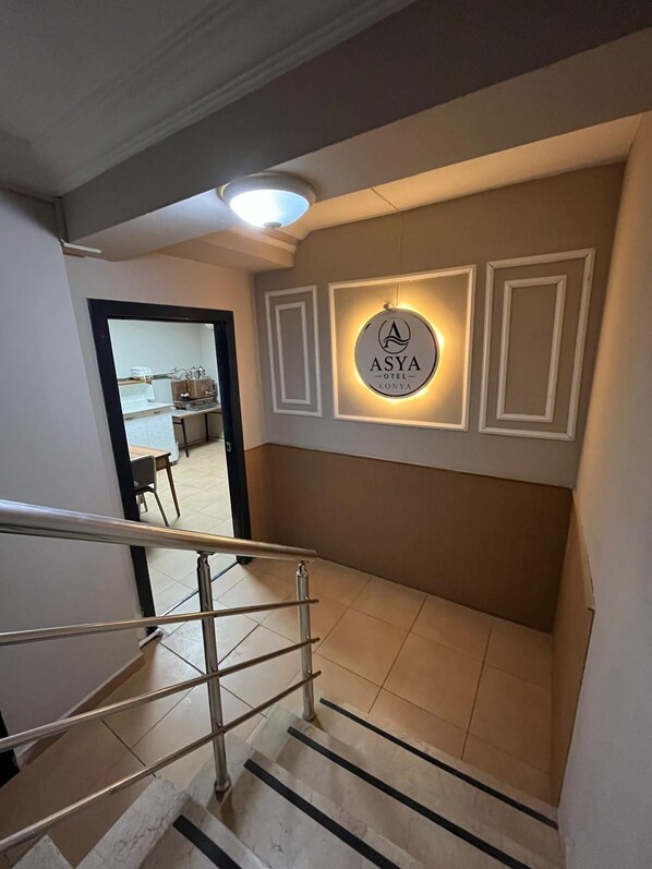 A hotel interior with a staircase, a wall-mounted sign, and a glimpse of a kitchen area.