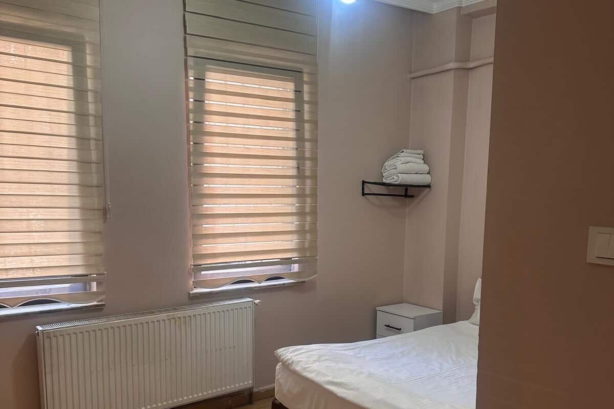 Un dormitorio con cama, radiador, ventana con persianas y una lámpara en el techo.