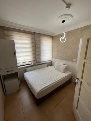 A bedroom with a bed, a radiator, a wardrobe, and a window with blinds.