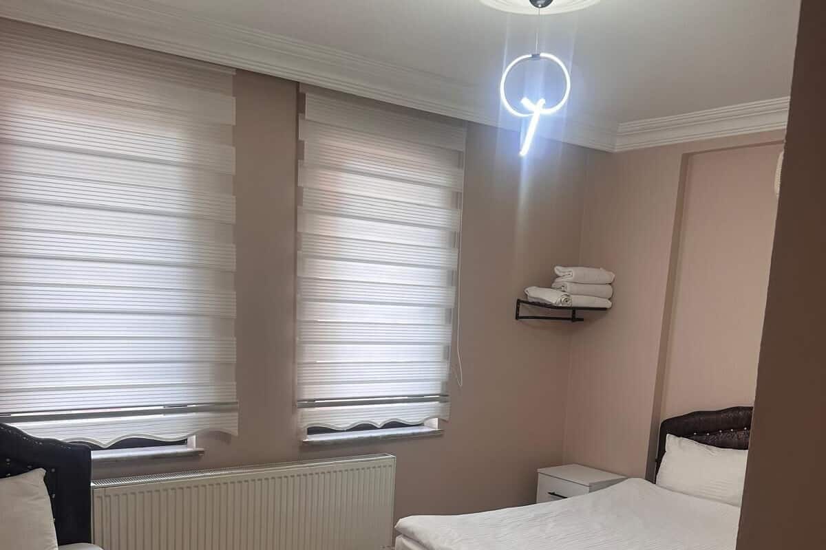 Habitación de hotel con dos camas, un radiador, una lámpara en el techo y un estante con toallas.