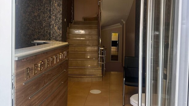 Un'area reception con una scrivania in legno con la scritta “RECEPTION”, una scala e una porta in vetro che dà su un'altra stanza.