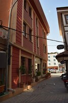 Una estrecha calle empedrada flanqueada por edificios rojos, una motocicleta estacionada y algunas macetas con plantas.