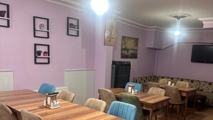 Un'area pranzo con diversi tavoli e sedie in legno, una televisione montata a muro e una ventola a soffitto.