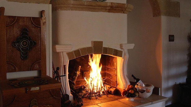 A fireplace with a fire, a wooden chest, and a fruit bowl with oranges and a bottle of wine. - La Ferula Casa Vacanze (Laterza)