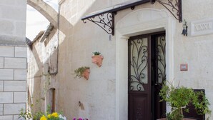 A building entrance with a stone facade, a dark wooden door, and a wrought iron gate. There are flower pots on the wall and a large potted plant in front. - La Ferula Casa Vacanze (Laterza)