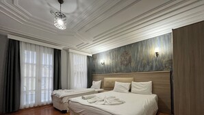 A hotel room with two beds, a wooden floor, a large window with curtains, and a decorative wall. - Jasmine Apartment (Istanbul)