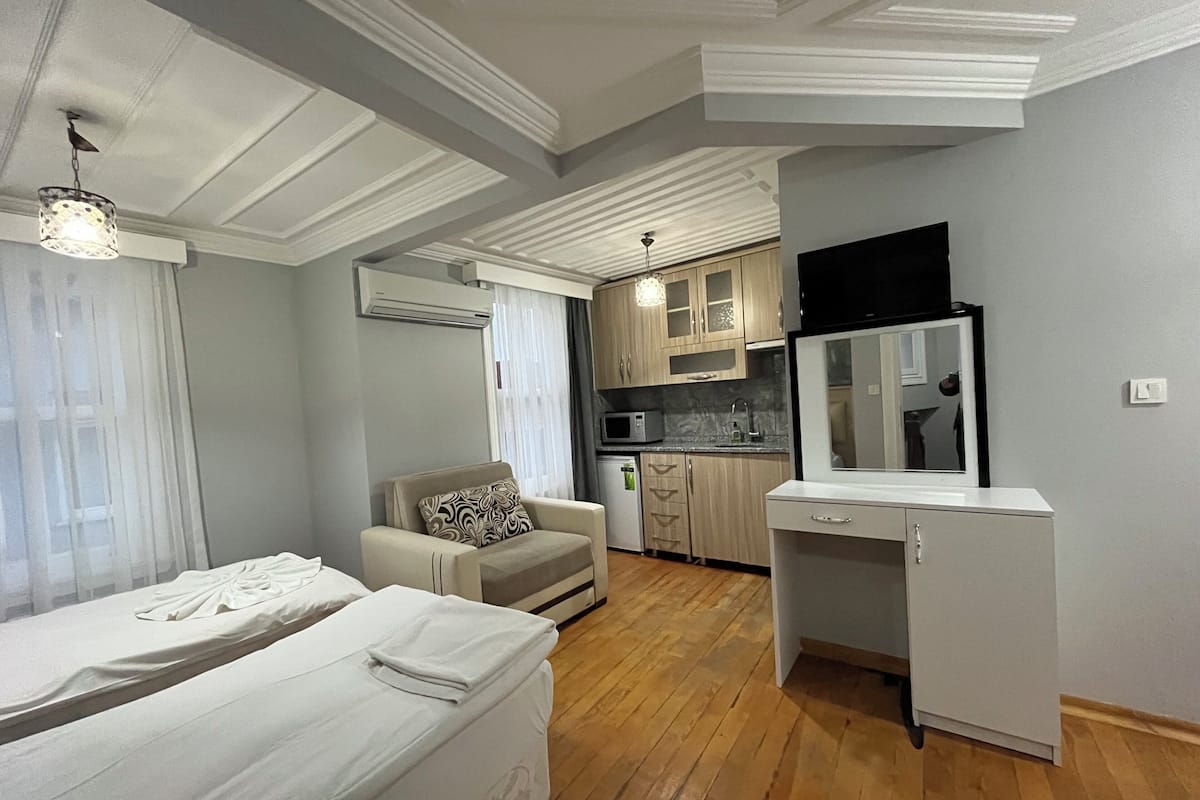 A compact hotel room with two beds, a sofa, a kitchenette, and a TV.