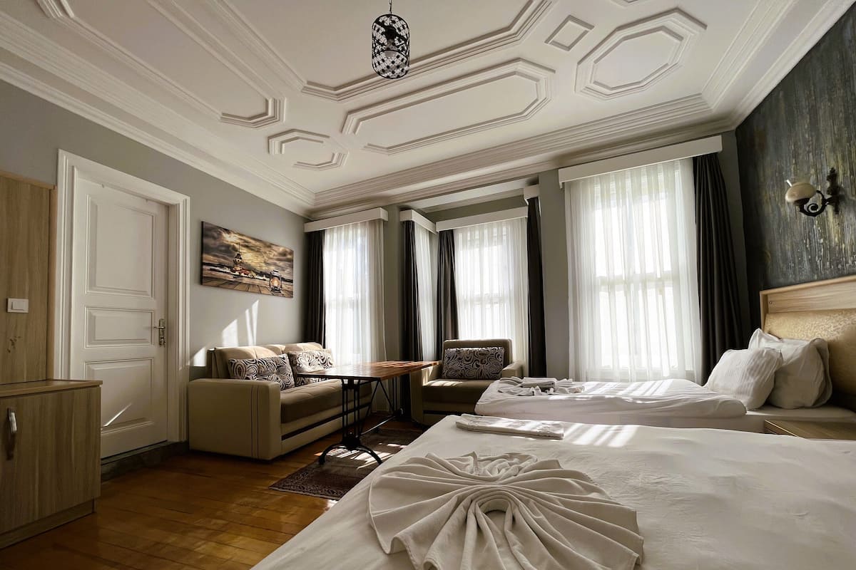 A hotel room with a large bed, a smaller bed, a sofa, a table, and a painting on the wall.