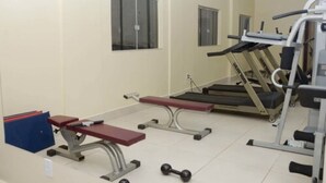 Ein Fitnessraum mit Trainingsgeräten, darunter Laufbänder, eine Bank und Kurzhanteln.