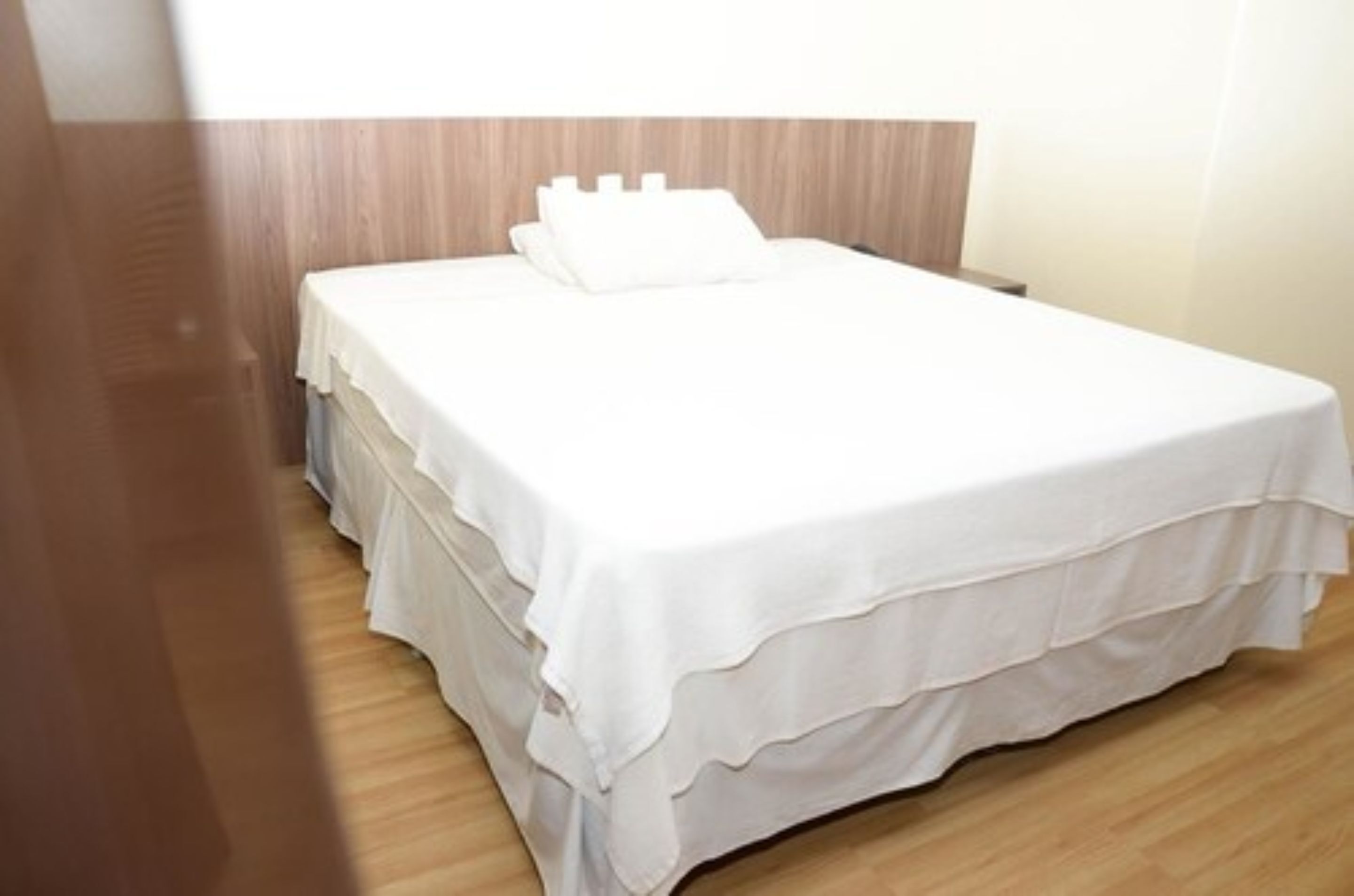 A neatly made bed with white bedding and a wooden headboard in a hotel room.