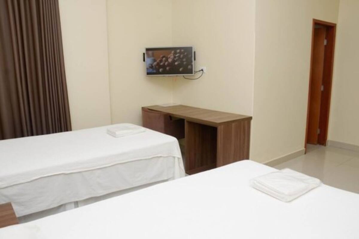 Ett hotellrum med två separata sängar, ett skrivbord i trä, en tv som är monterad på väggen och en dörr som leder till ett annat rum.