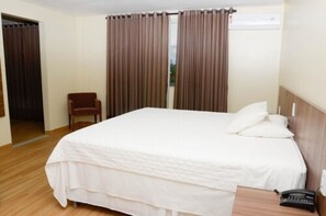 Une chambre d’hôtel avec un lit simple, une chaise, une table de chevet avec un téléphone et des rideaux marron.