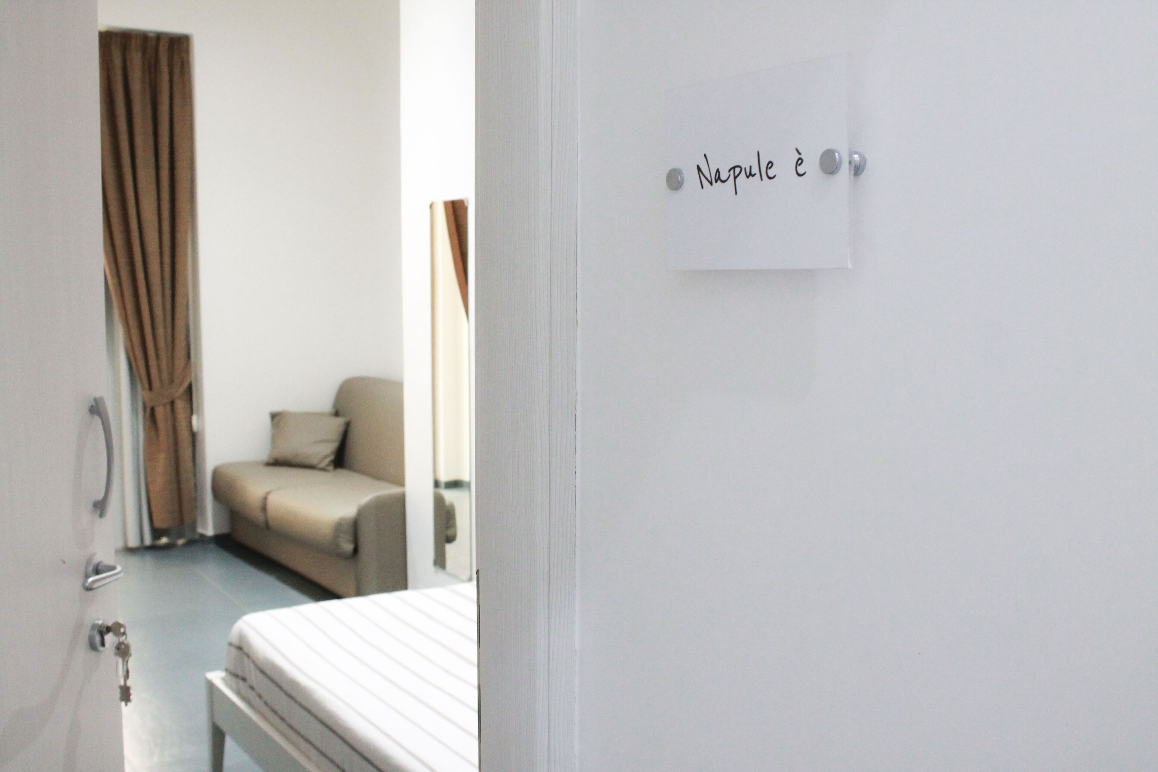 A hotel room with a bed, a chair, a door, and a wall with a sign.