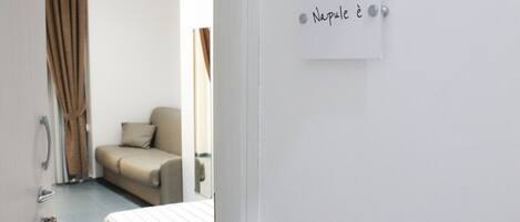 A hotel room with a bed, a chair, a door, and a wall with a sign.