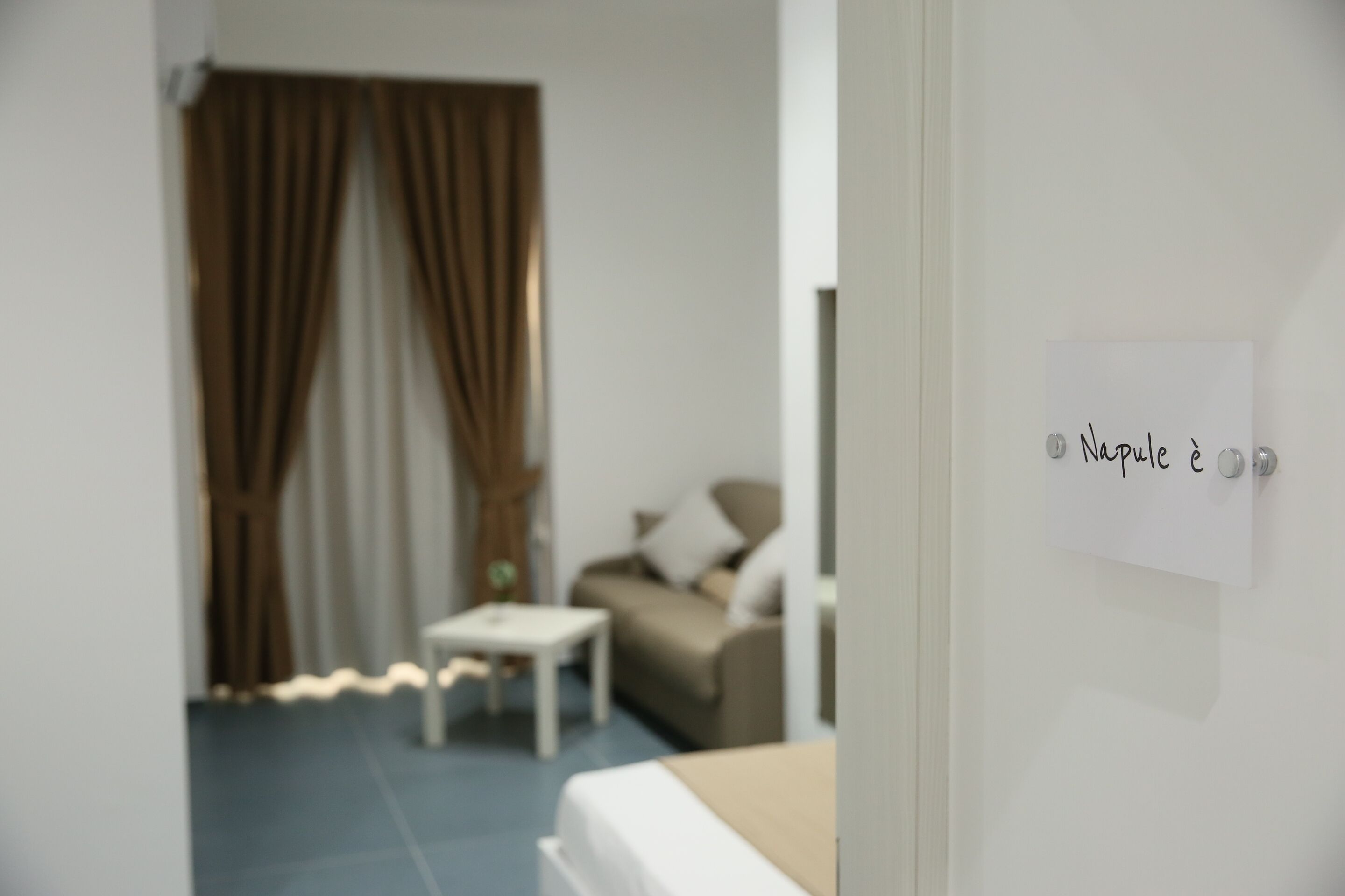 A bedroom with a bed, a small table, a sofa, and a curtain.