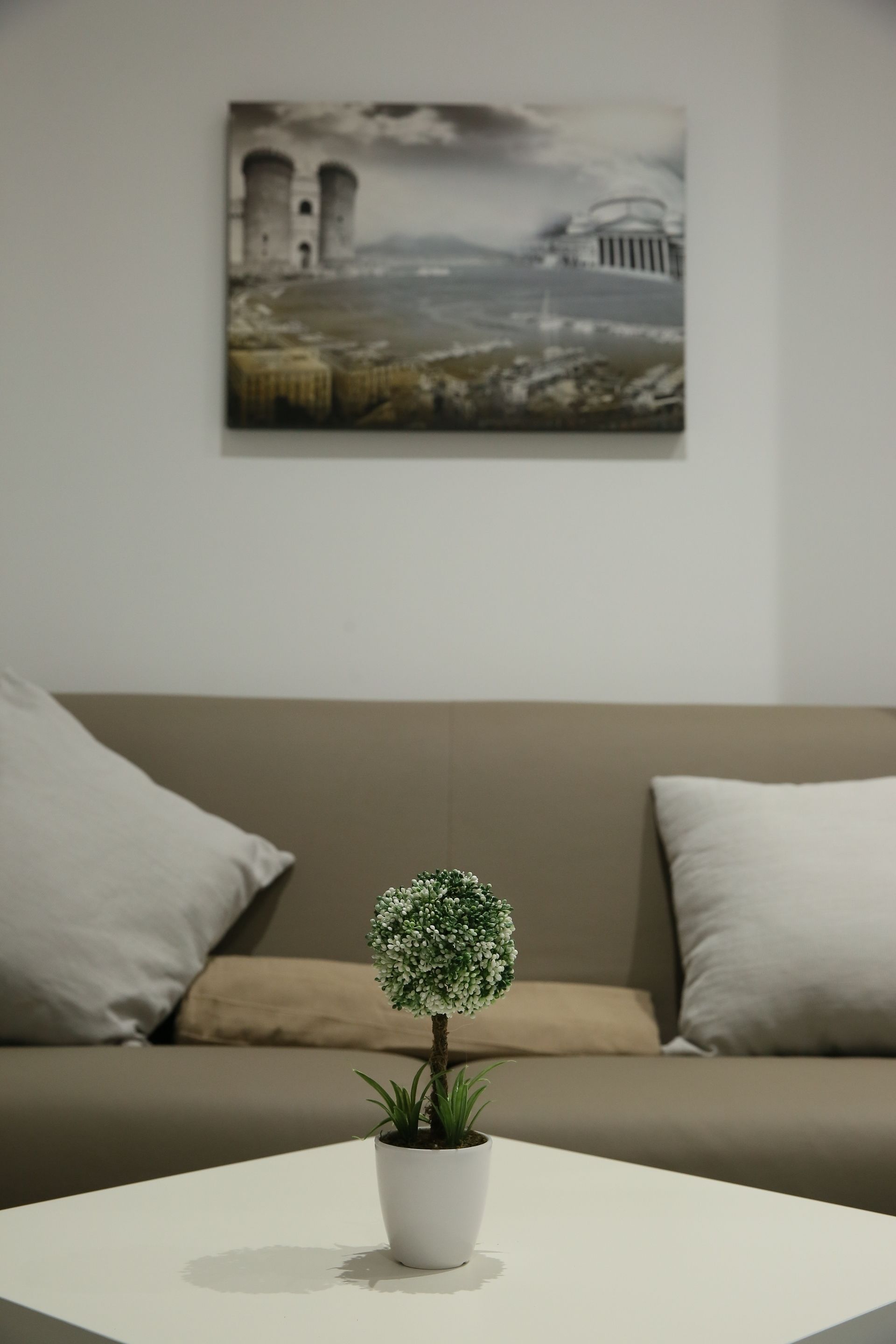 Un salón moderno con una mesa redonda blanca, una planta en maceta y un cuadro de un edificio histórico en la pared.