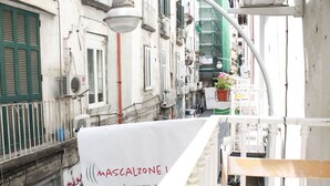 Una calle urbana estrecha con edificios, un estandarte blanco con texto y una farola.