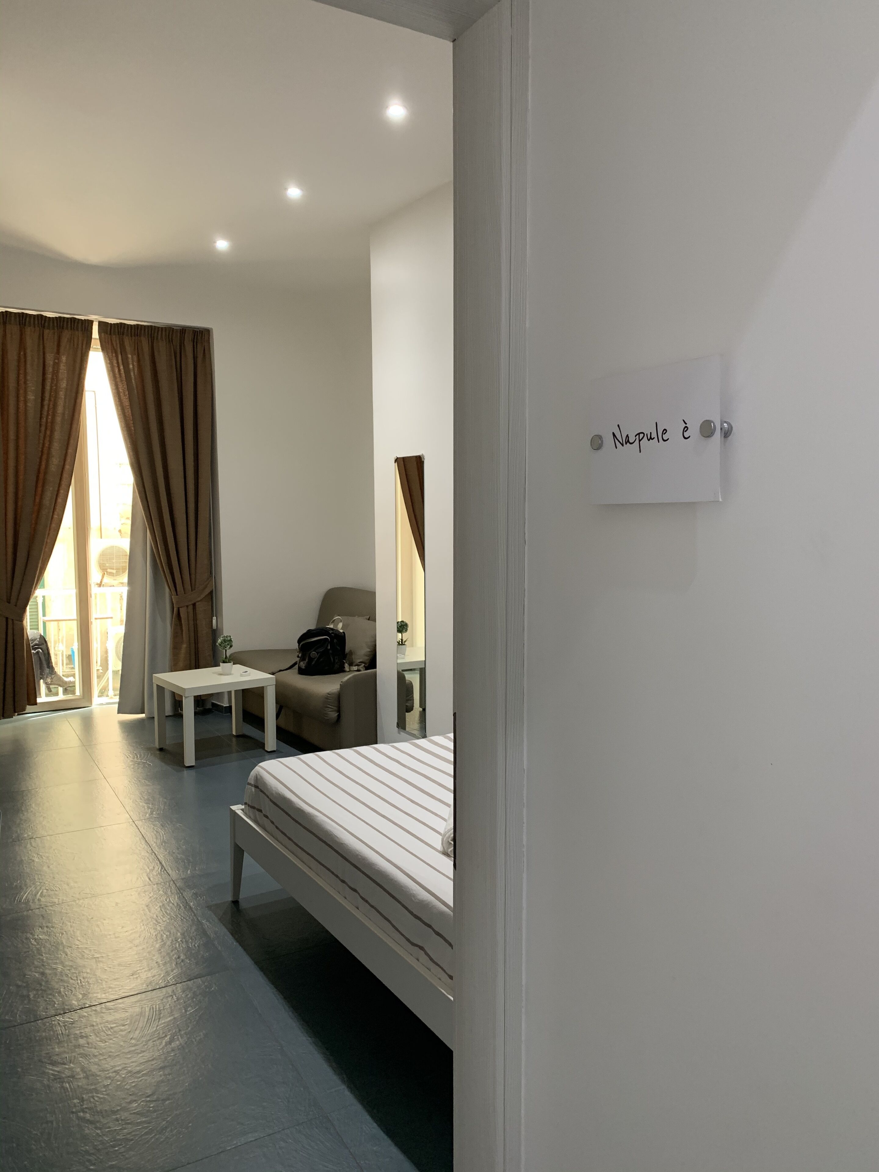 A hotel room with a bed, a chair, a small table, and a sign on the wall.