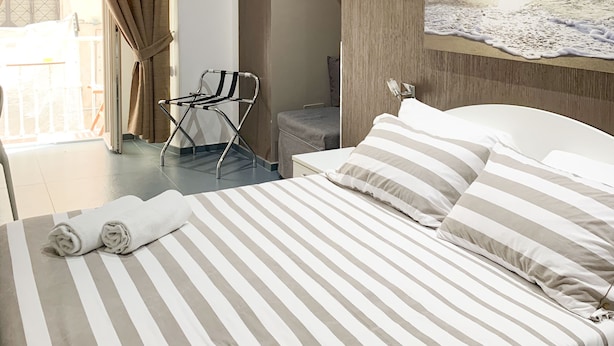 Habitación de hotel con cama, un cuadro de un atardecer, unidad de aire acondicionado y vistas al balcón exterior.