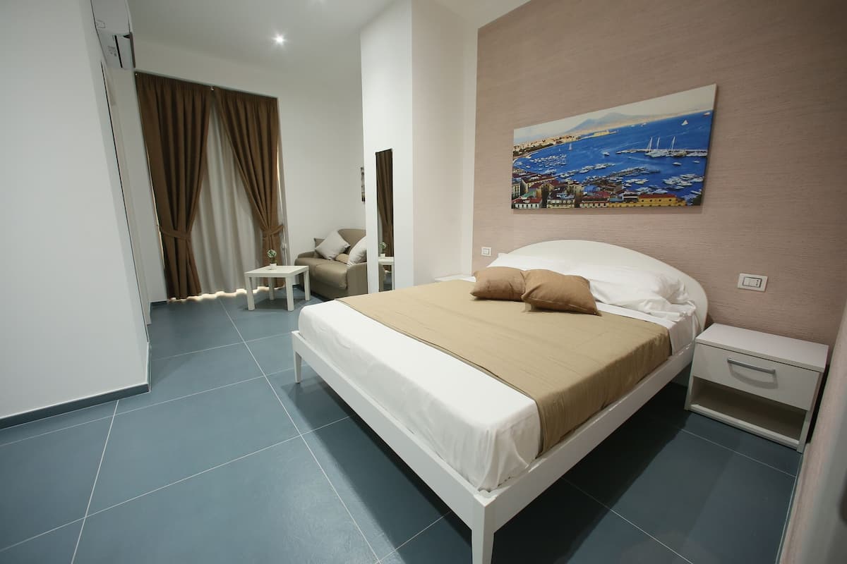 A hotel room with a bed, a nightstand, a chair, and a painting on the wall.