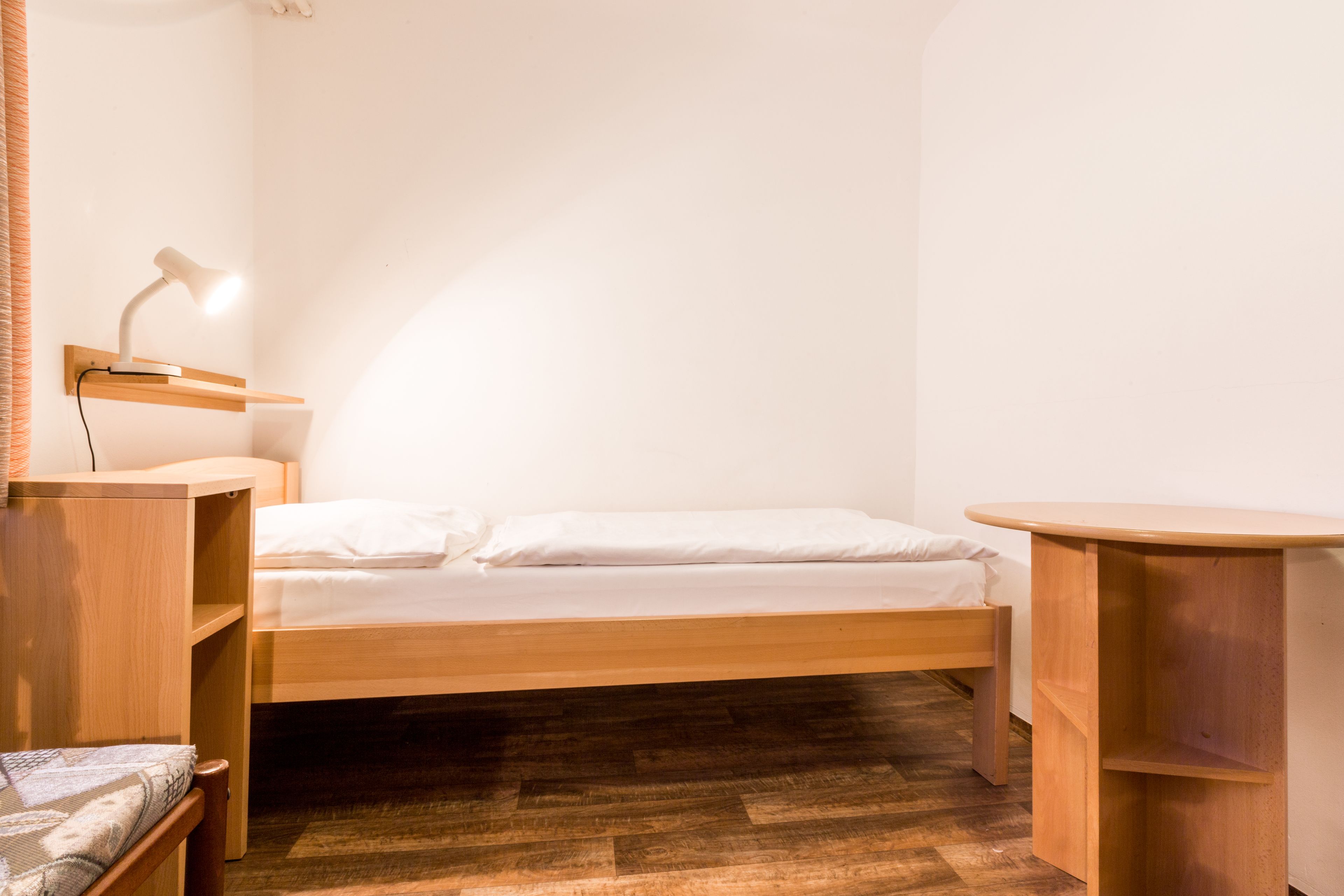 A small, neatly organized room with a single bed, a desk, and a chair.