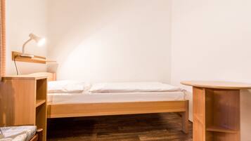 A small, neatly organized room with a single bed, a desk, and a chair.