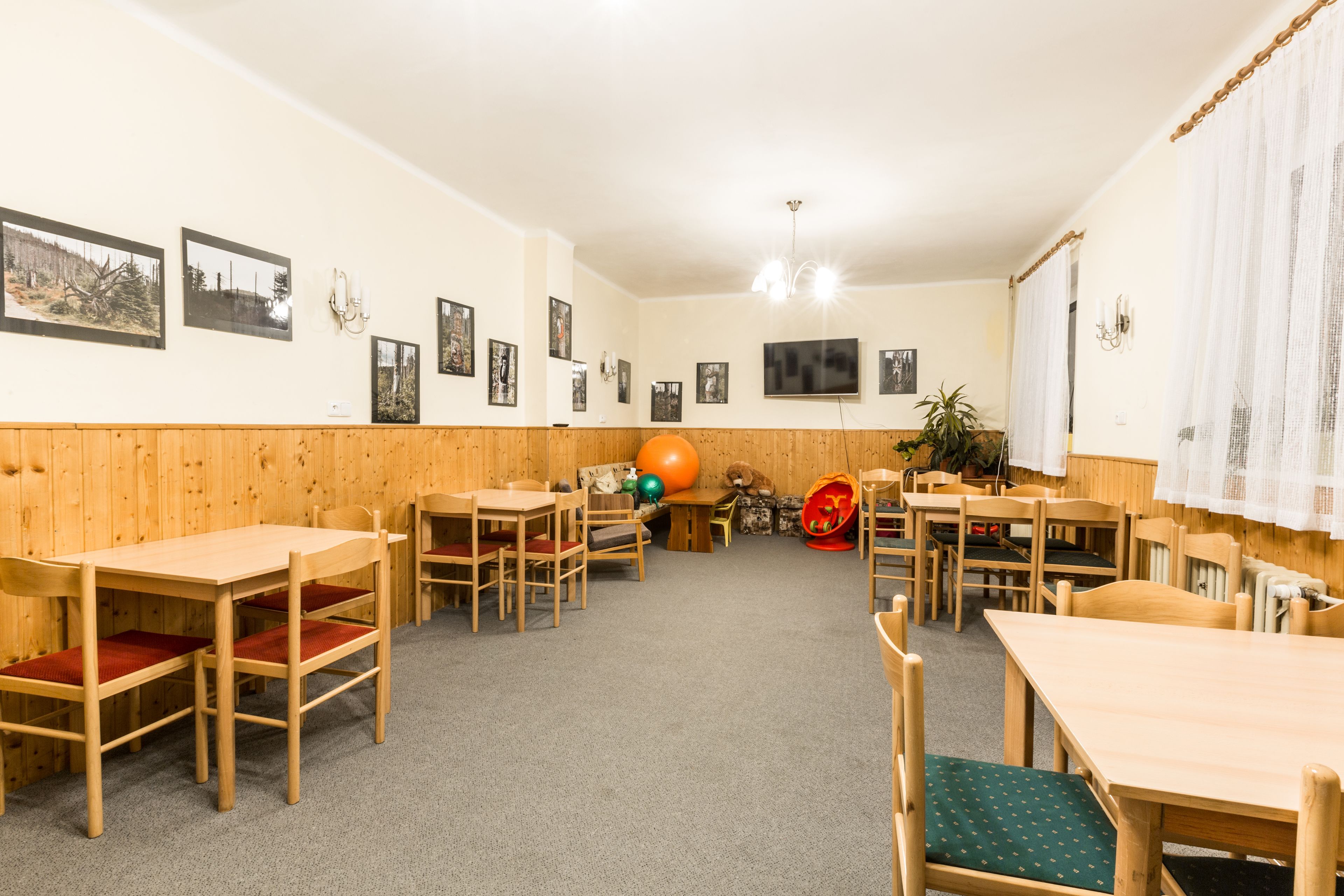 A dining area with wooden tables and chairs, a television mounted on the wall, and framed pictures on the walls.