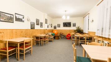 A dining area with wooden tables and chairs, a television mounted on the wall, and framed pictures on the walls.