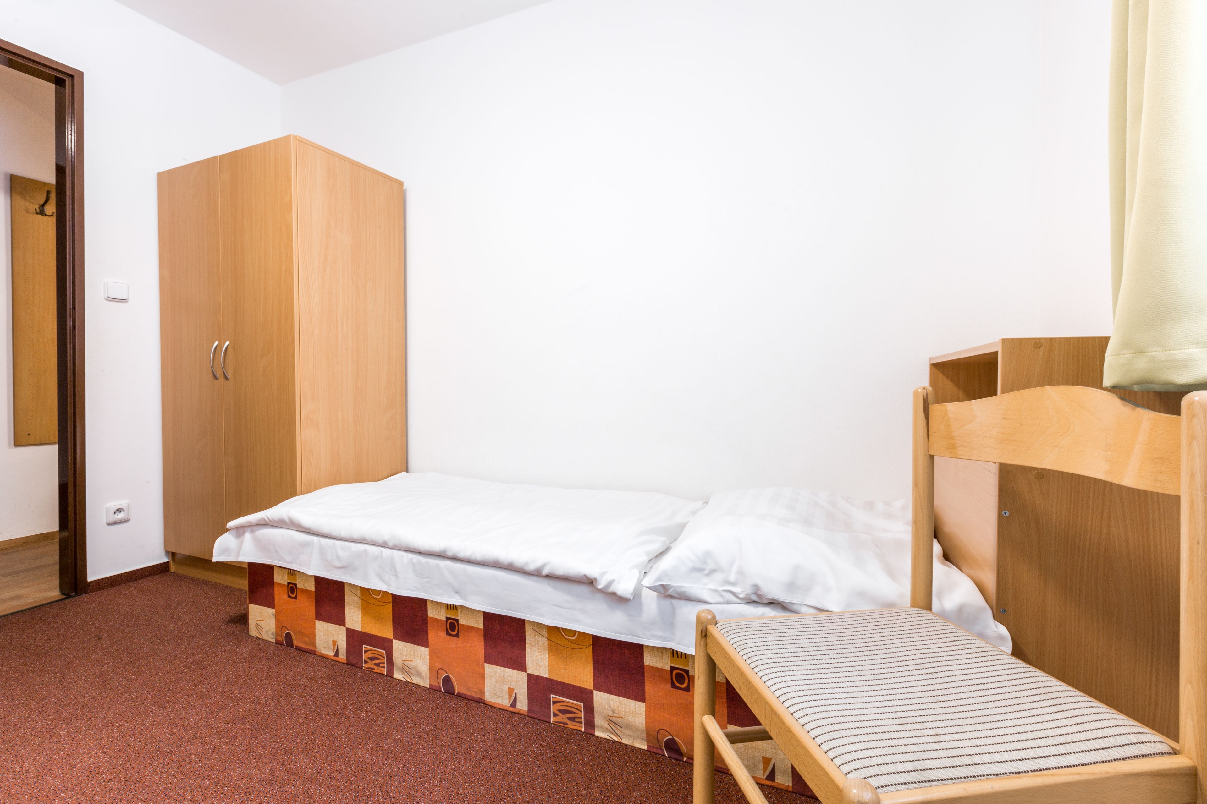 Un alojamiento pequeño y de una sola habitación con una cama litera, un armario de madera y un cubrecolchón estampado en cuadros.