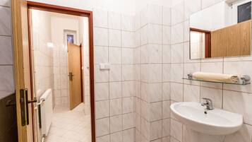 Un baño con un lavamanos blanco, un espejo y un estante de vidrio con toallas.