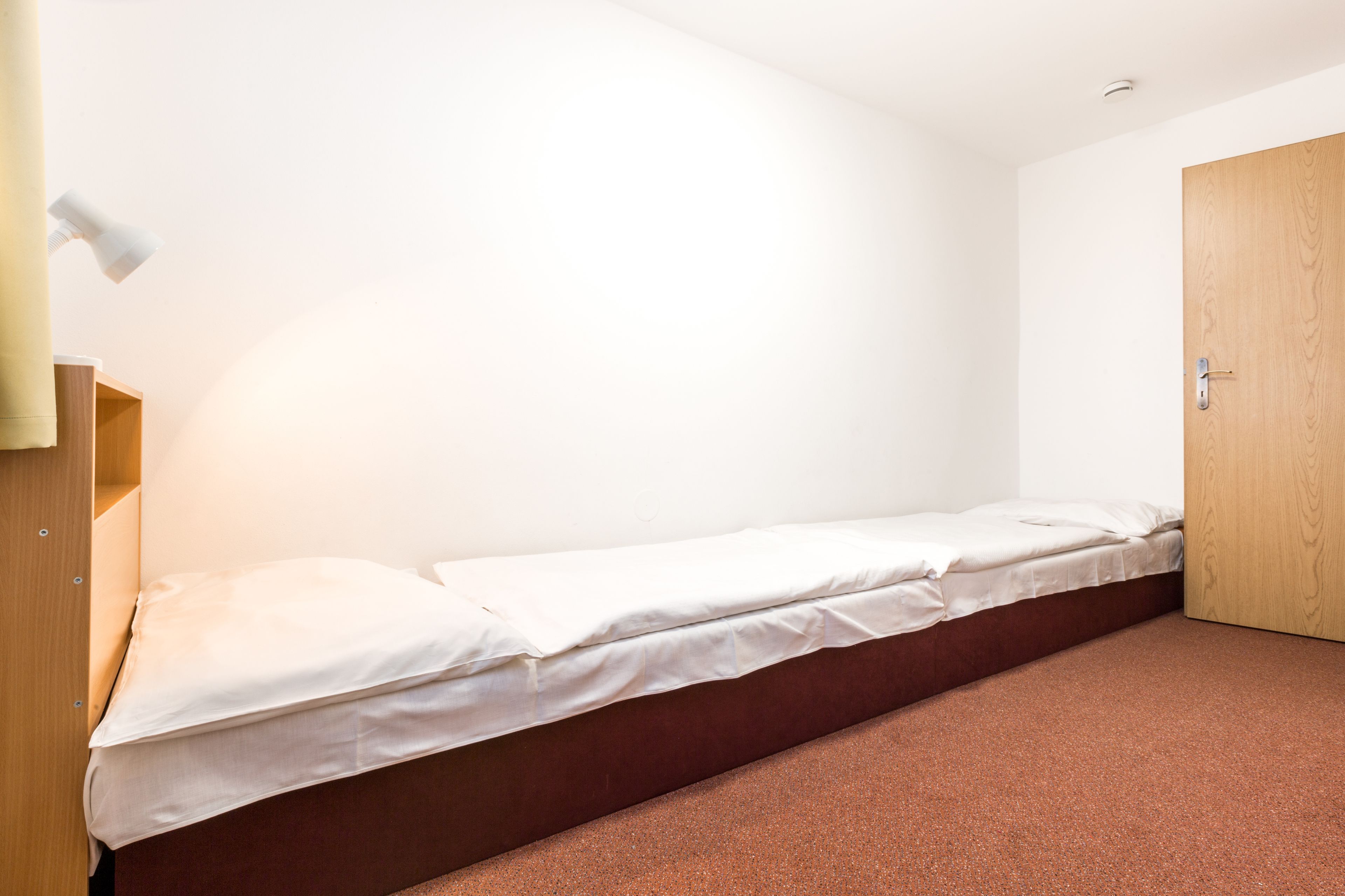 A single bed with a wooden headboard, a small bedside table, and a wardrobe.