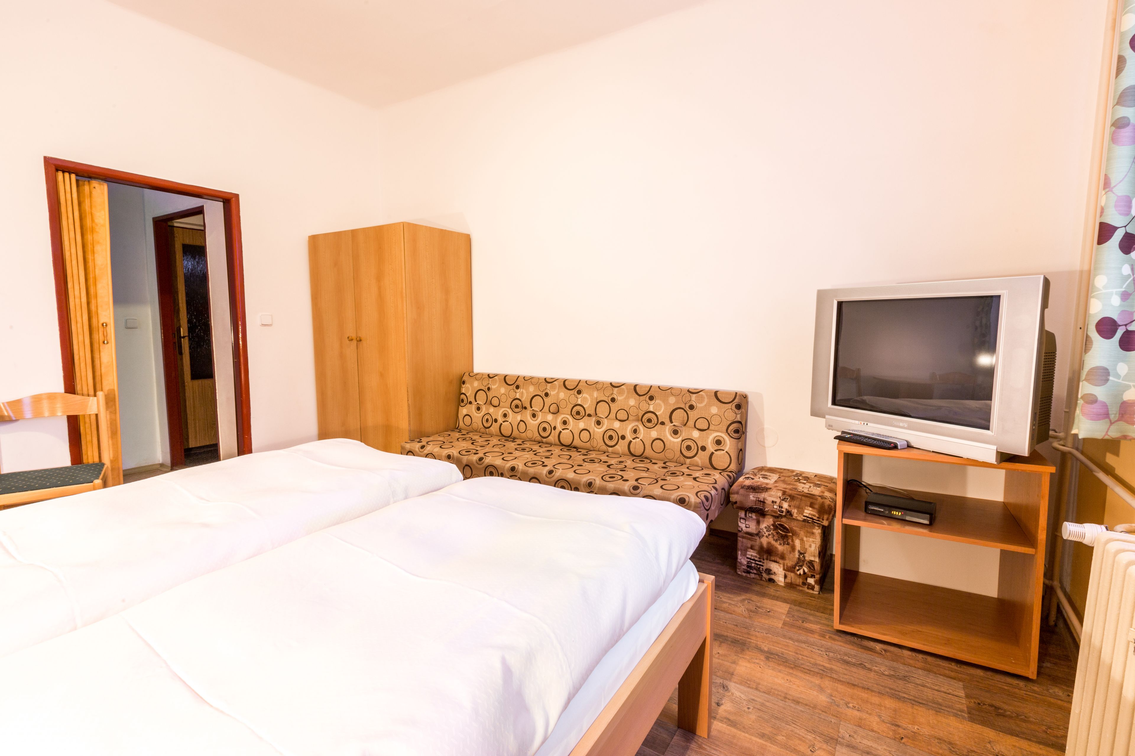 Een slaapkamer met een bed, een houten garderobe, een bank, een televisie en een klein kastje.