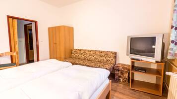 Een slaapkamer met een bed, een houten garderobe, een bank, een televisie en een klein kastje.