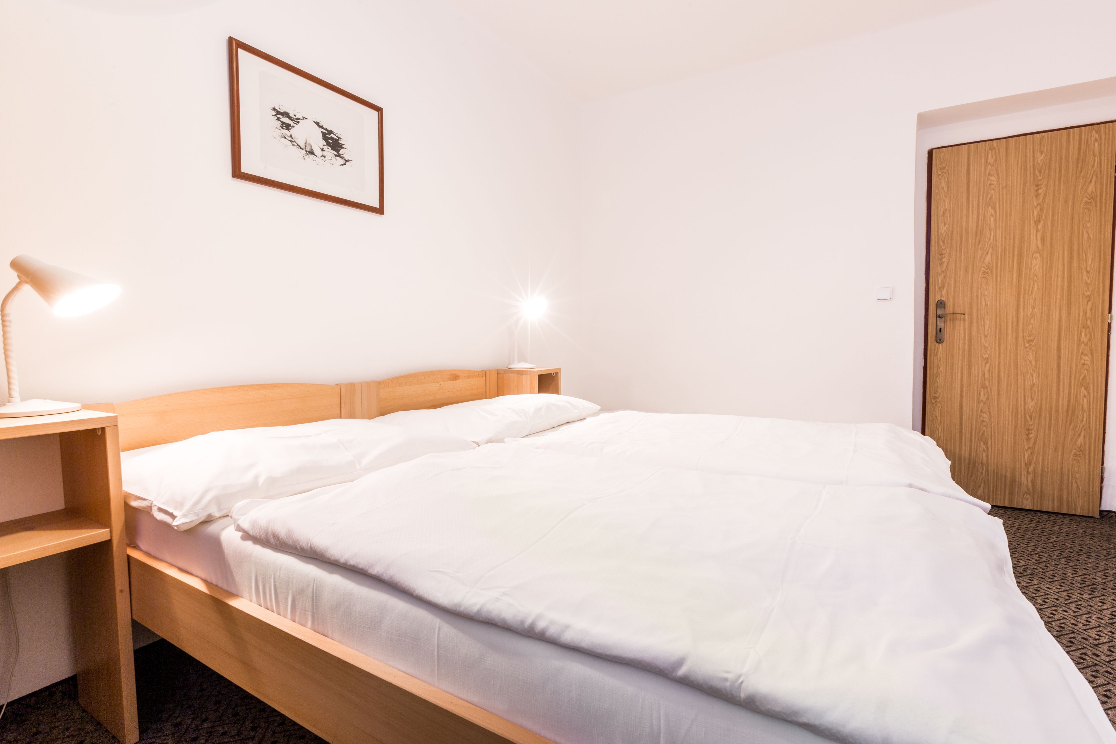 Een net opgemaakt bed met witte lakens en twee bedlampjes.