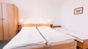 A room with two wooden beds, a wardrobe, and a bedside table with a lamp.