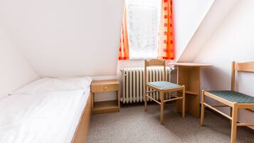 A bedroom with a bed, a desk, a chair, and a window with curtains.