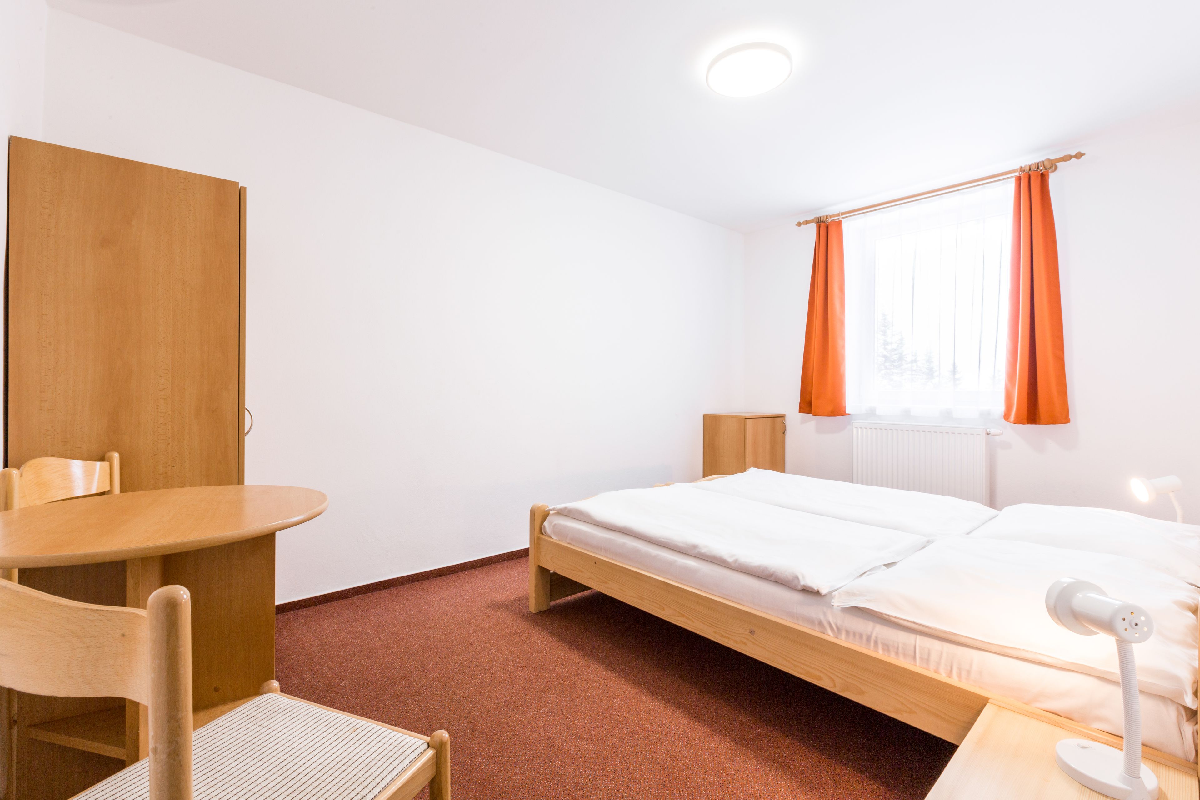 Una habitación con cama, escritorio, silla y ventana con cortinas.