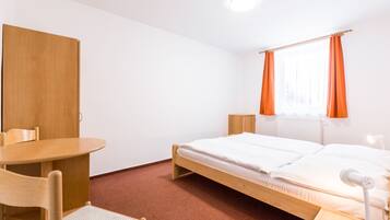 Una habitación con cama, escritorio, silla y ventana con cortinas.