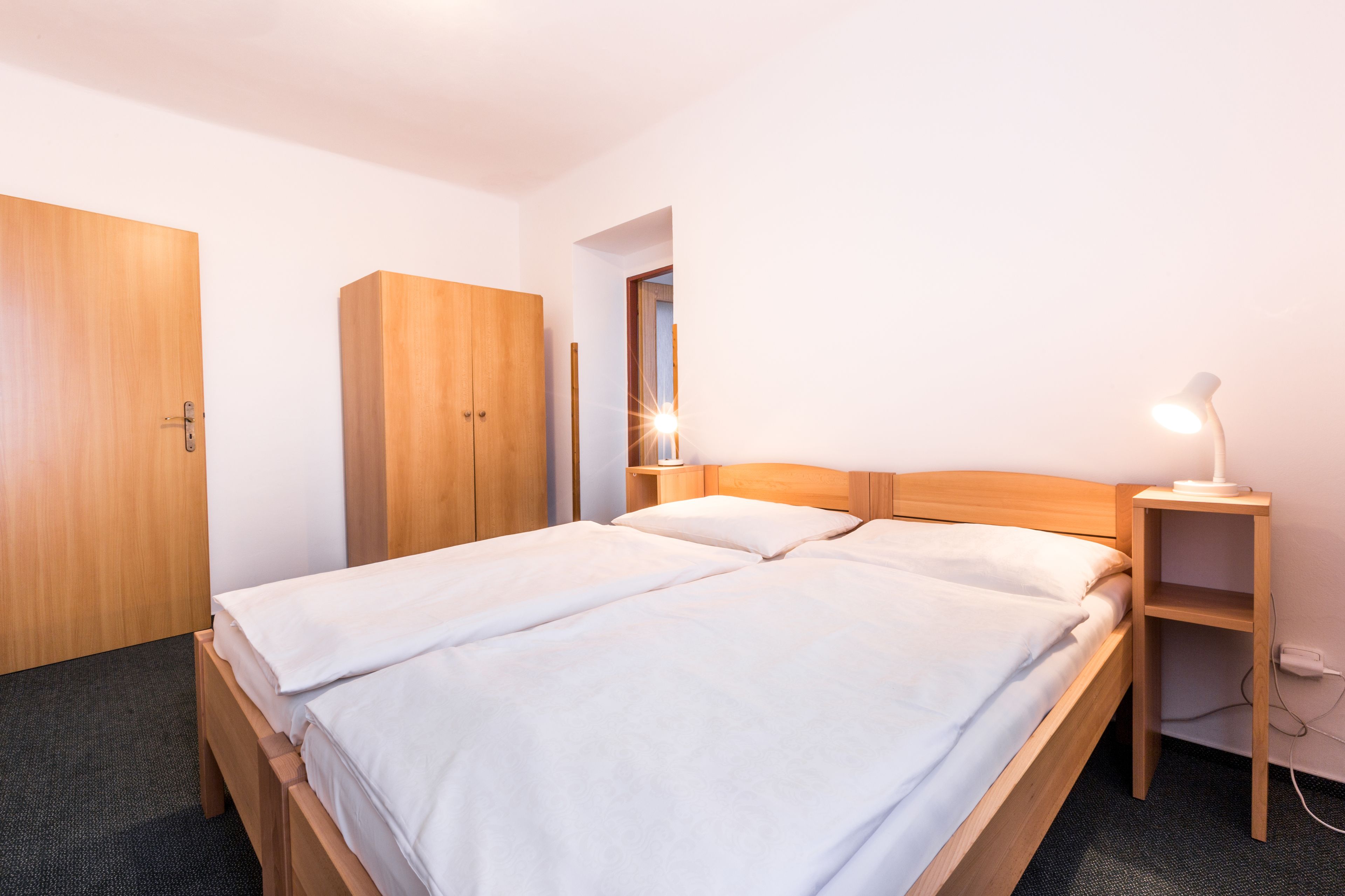 A double bed with a wooden headboard, a bedside table with a lamp, and a wardrobe.