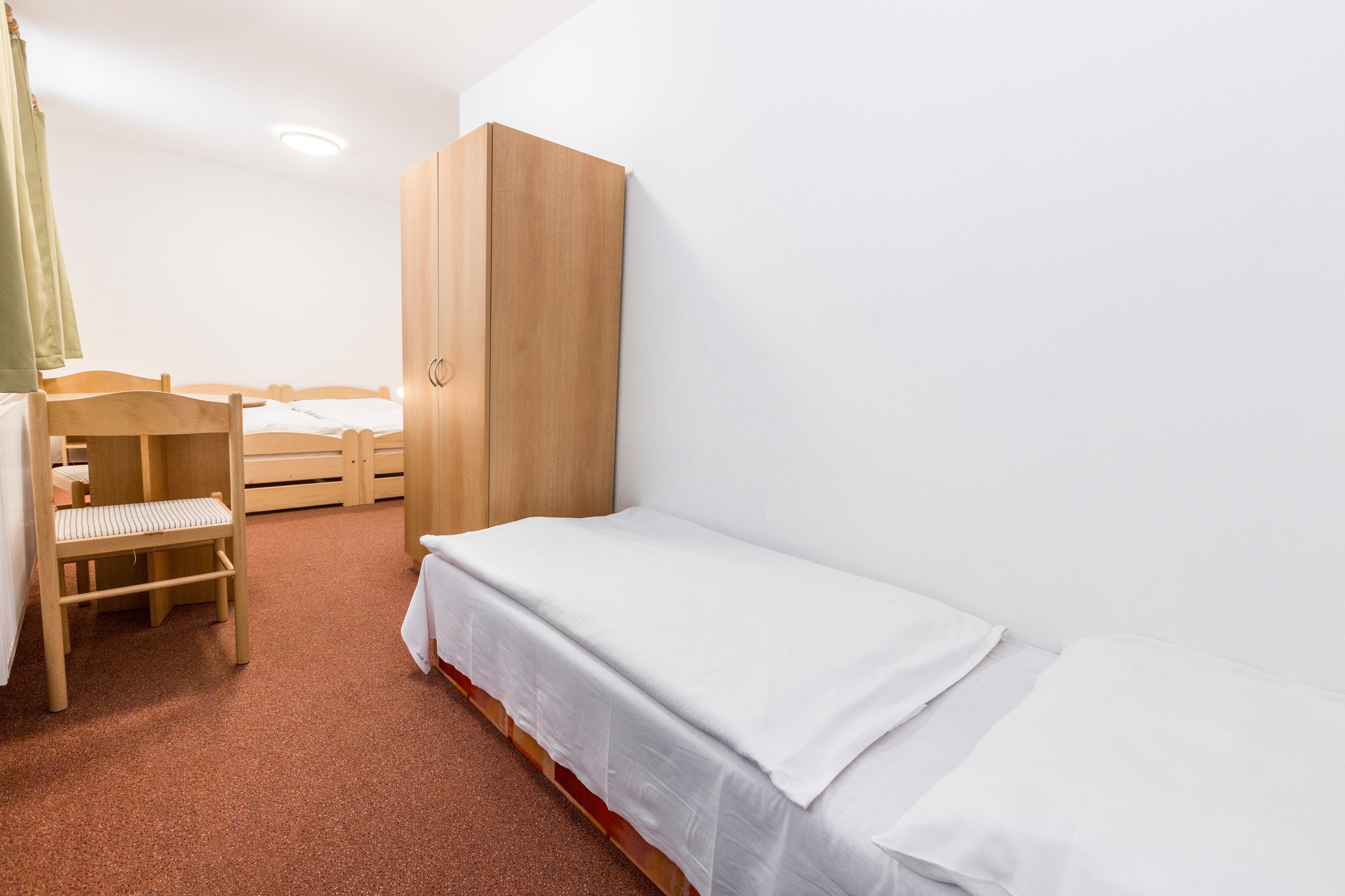 A small, clean room with a single bed, a wooden wardrobe, and a bench.