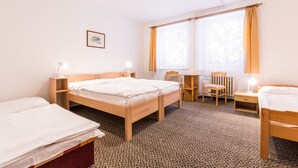 Habitación de hotel con dos camas individuales, un escritorio de madera con silla, una mesita y un radiador.