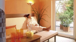 A spa room with a massage table, a potted plant, and a glass of yellow liquid. - Hotel Bei Den Tongruben (Neuberg)