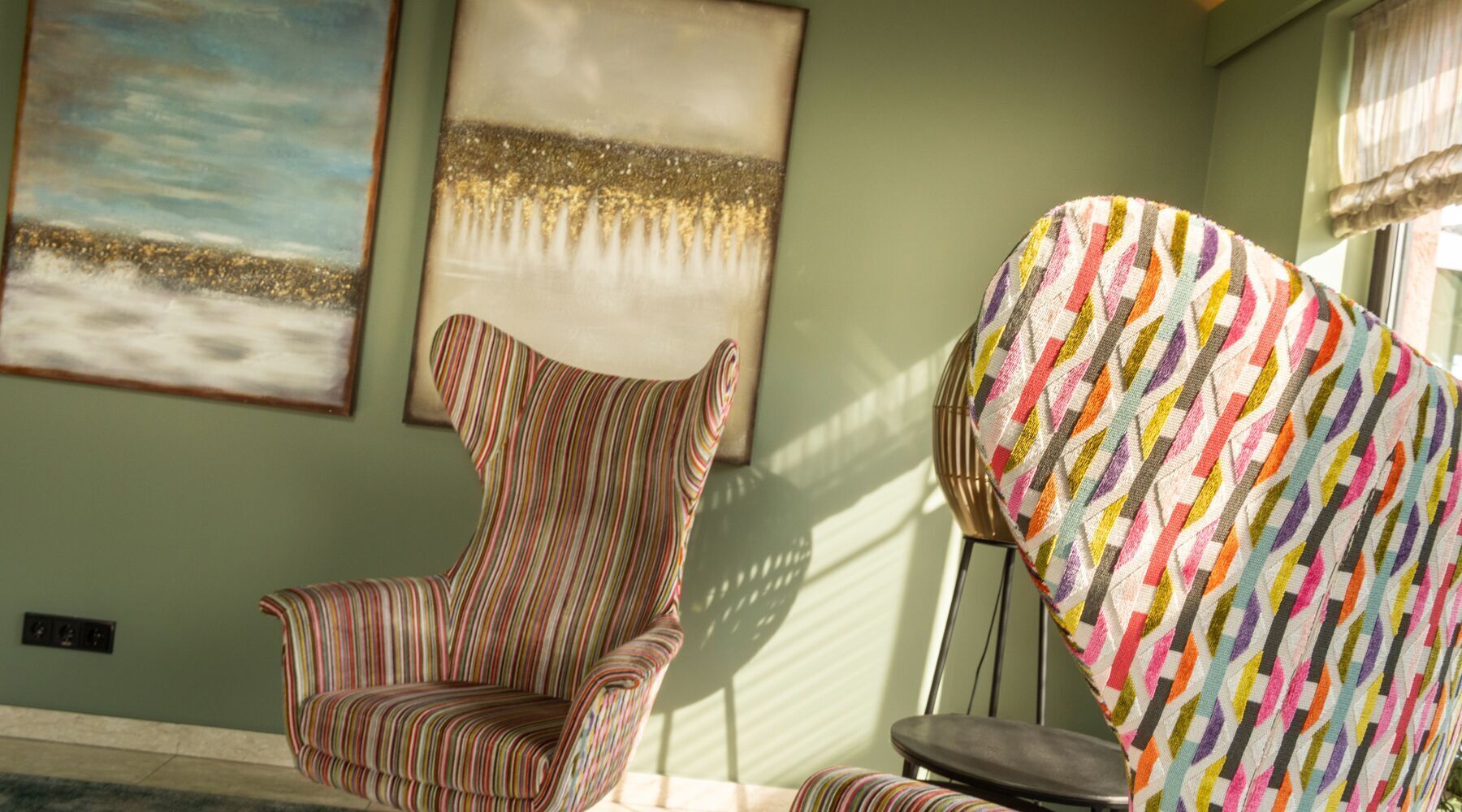 Un fauteuil à rayures et un fauteuil aux couleurs vives se trouvent dans une pièce dont les murs sont ornés d’œuvres d’art.