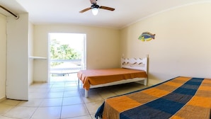 Un dormitorio con cama, ventilador de techo, ventana y balcón.