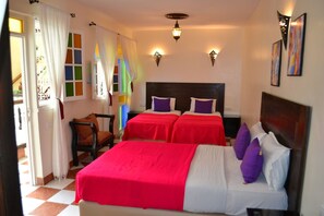Habitación de hotel con dos camas, cabecero de madera, una silla y un ventanal con vidrios de colores.